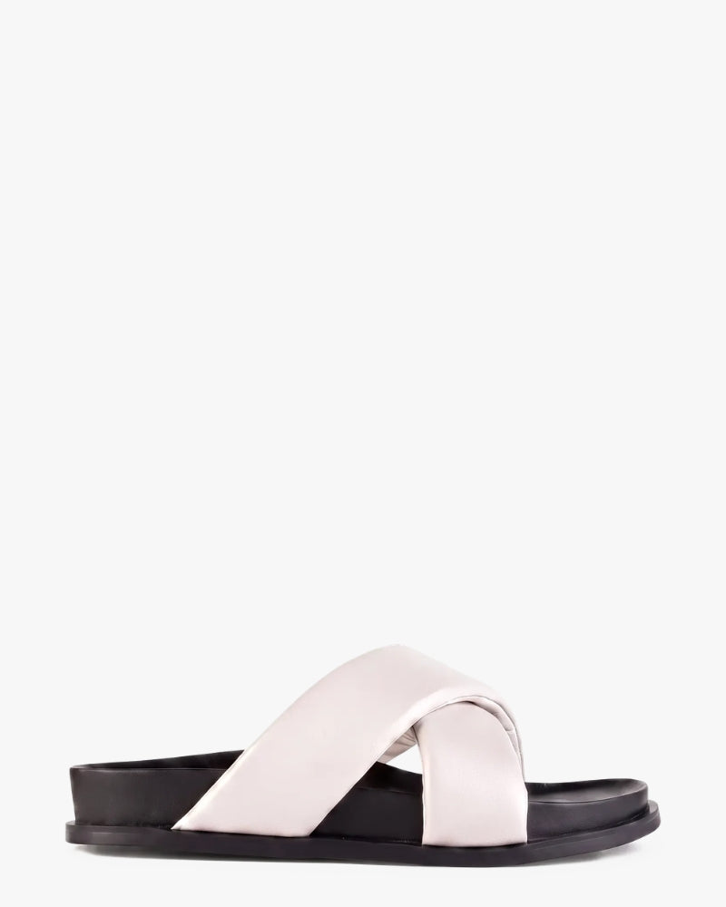 A minimalist slide sandal featuring wide, crisscrossing straps set on a black platform sole, shown against a plain white background.